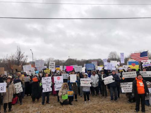 protesters in winter gear carrying signs protesting Trump
